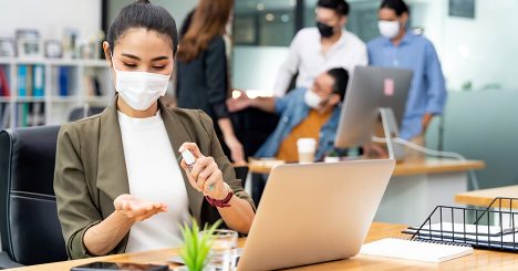 Woman In Mask At Work Using Hand Sanitizer