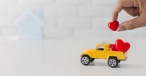 Hand Placing Hearts On Toy Truck In Front Of Toy House