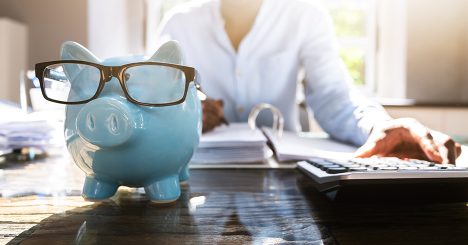 Blue Piggy Bank With Glasses In Front Of Woman Working In Office